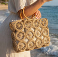 Woven handbag with circular patterns held by a person on a beach.