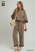 Woman wearing a brown outfit holding a bag and an apple against a plain background