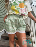Person wearing a white t-shirt with fruit graphics and green plaid shorts on a wooden staircase.