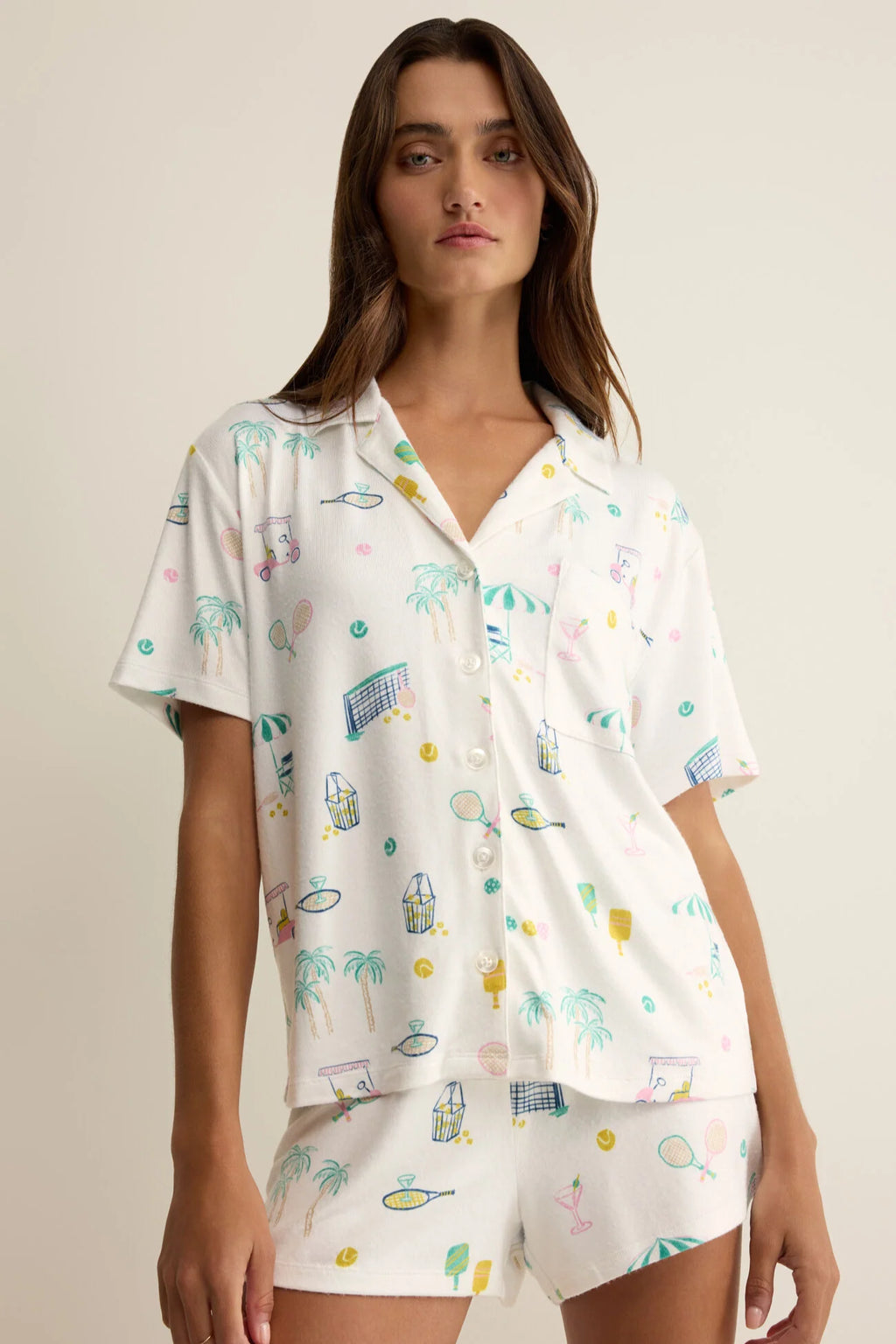 Woman wearing a white pajama set with colorful patterns on a beige background