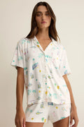 Woman wearing a white pajama set with colorful patterns on a beige background