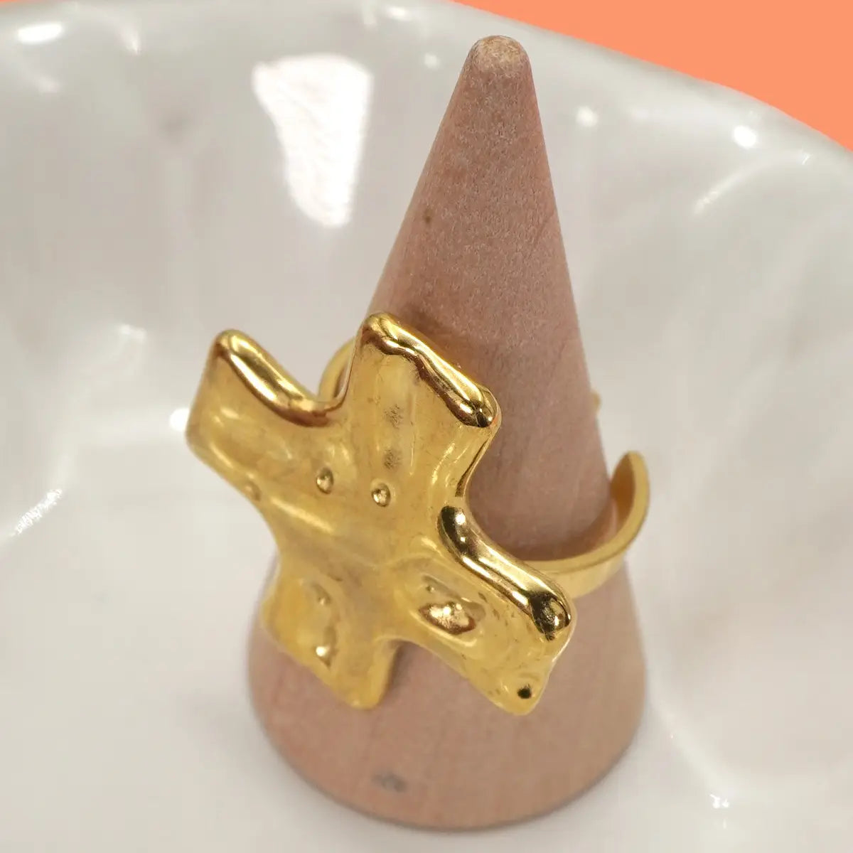 Gold star-shaped ring on a pink cone against a white background