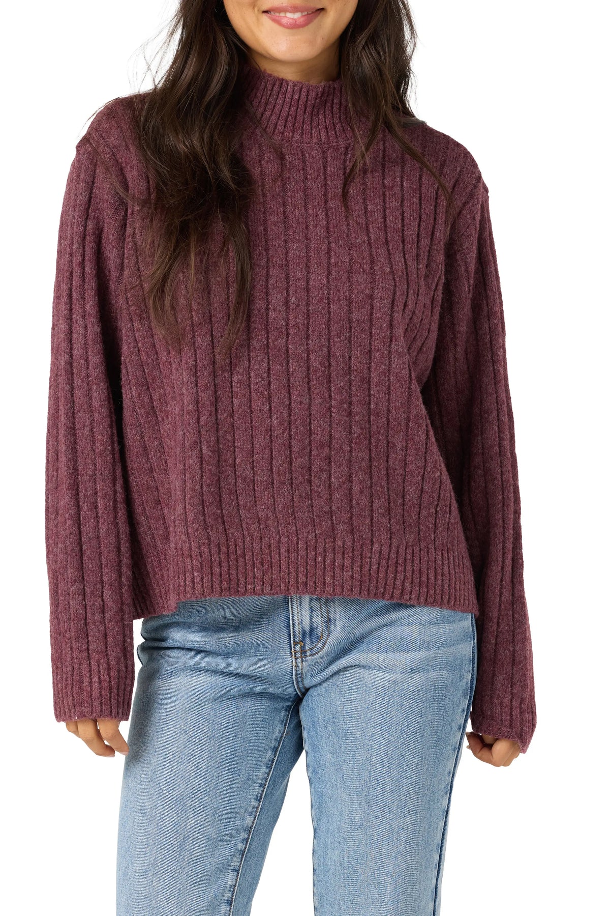A woman wearing a ribbed knit mock neck sweater in a heathered burgundy color, paired with light blue jeans, against a plain white background.