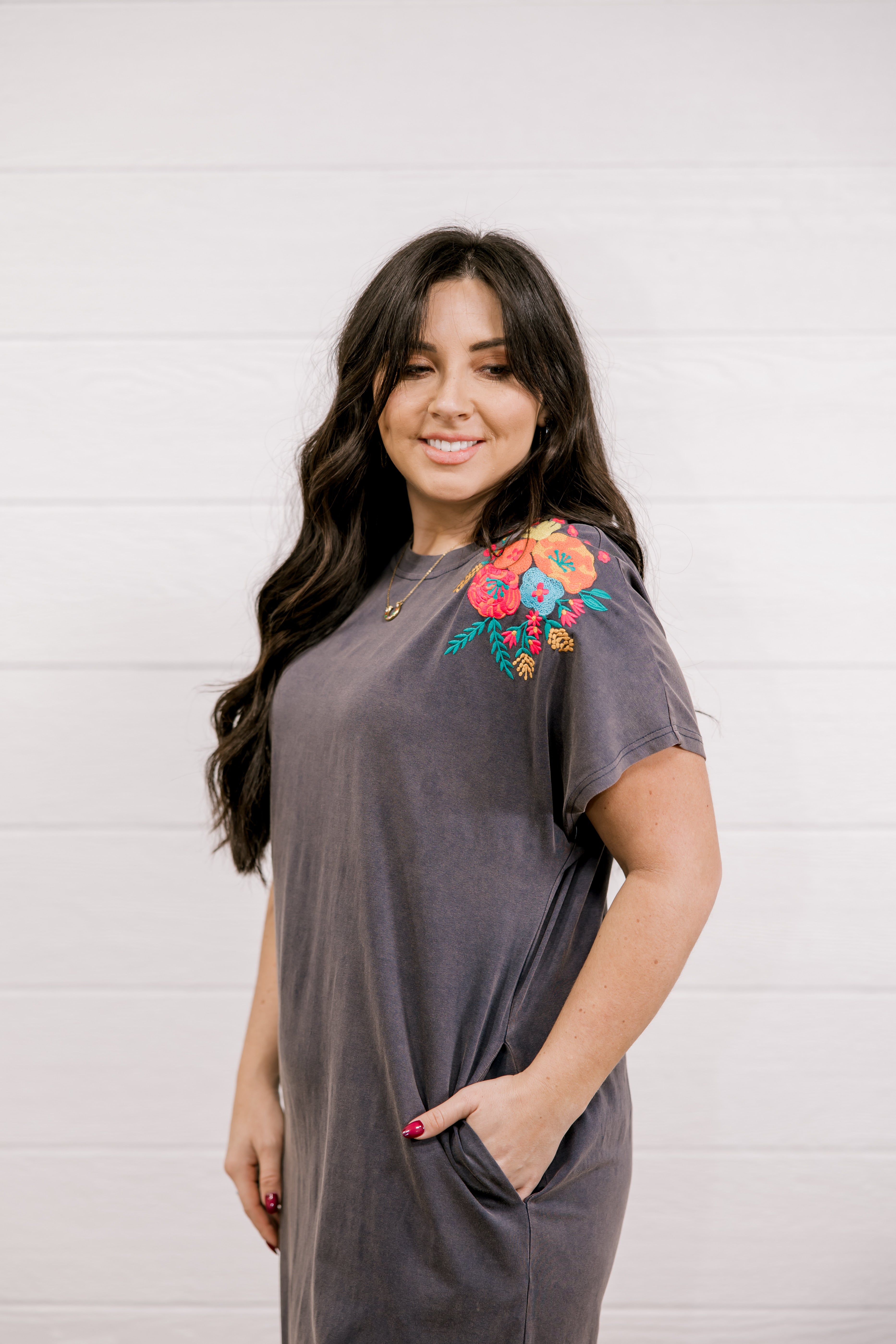 Woman wearing a gray dress with colorful floral embroidery against a white background