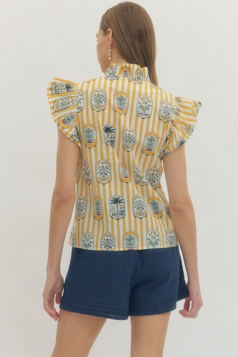 Woman wearing a yellow patterned top and navy shorts on a white background