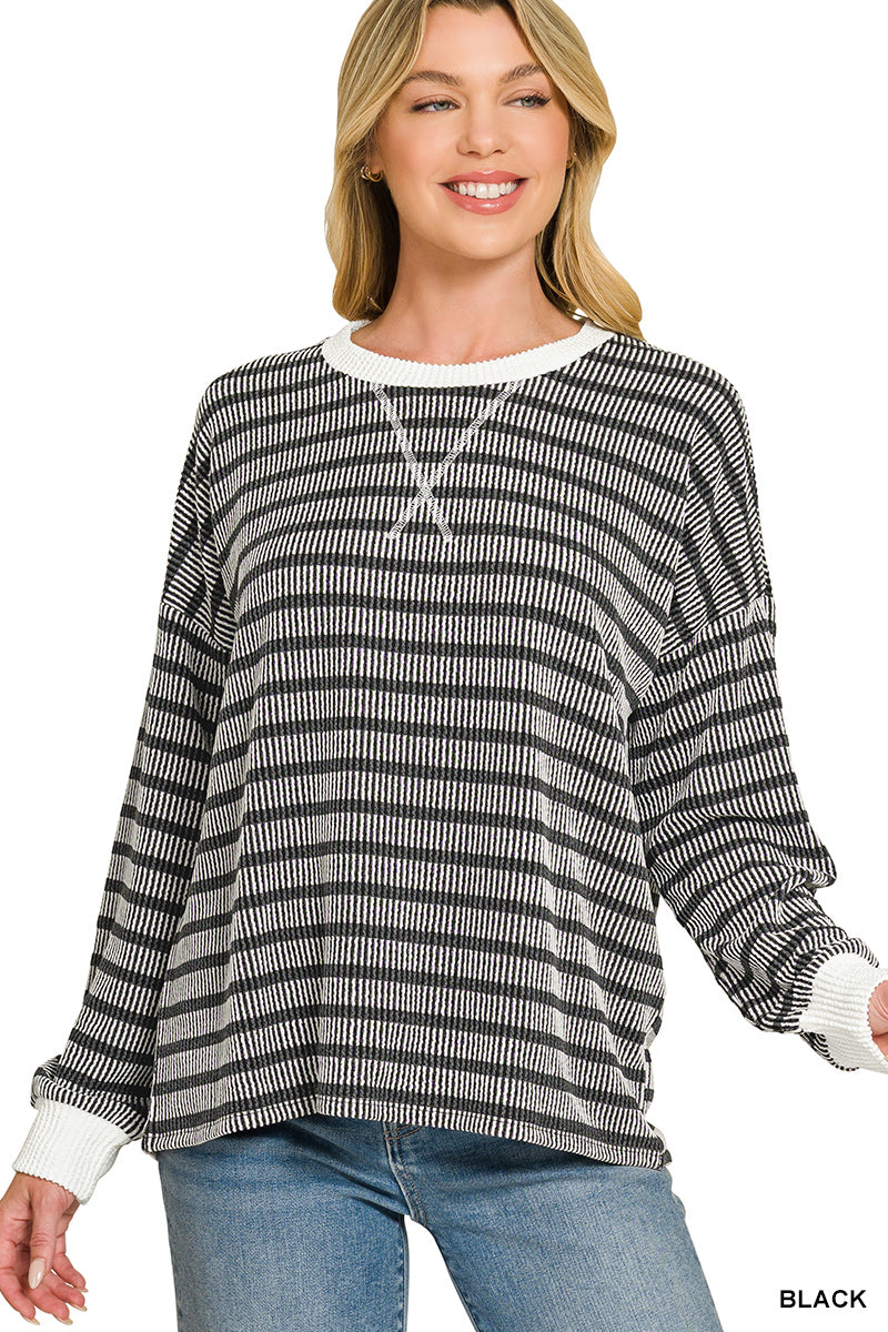 A woman wearing a black and white horizontally striped knit long-sleeve top with white ribbed cuffs and collar, paired with blue jeans. The image has a 'PLUS' label in the top right and 'BLACK' text in the bottom right, set against a plain white background.