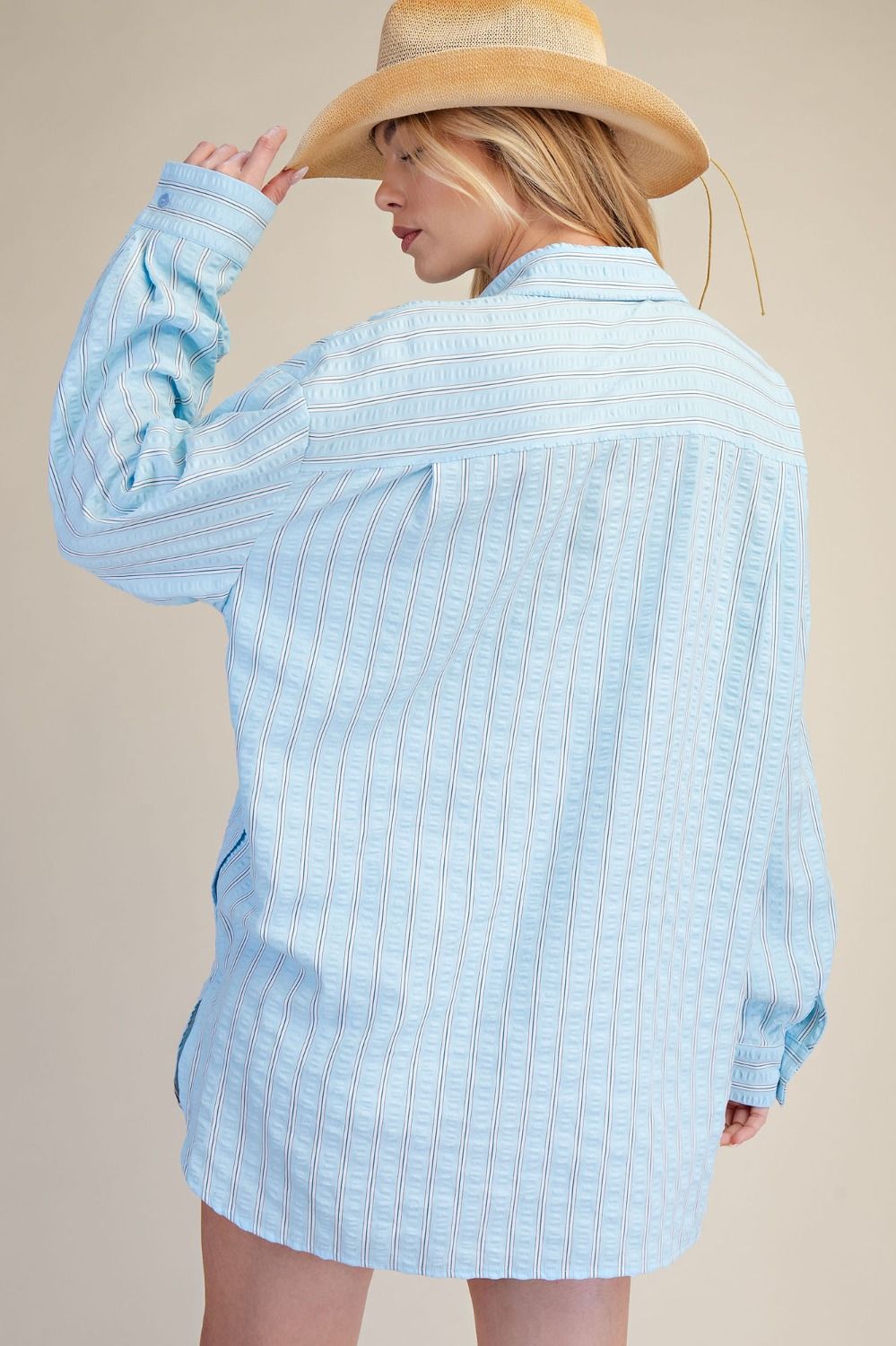 Woman wearing a light blue checkered shirt and a wide-brimmed hat on a beige background