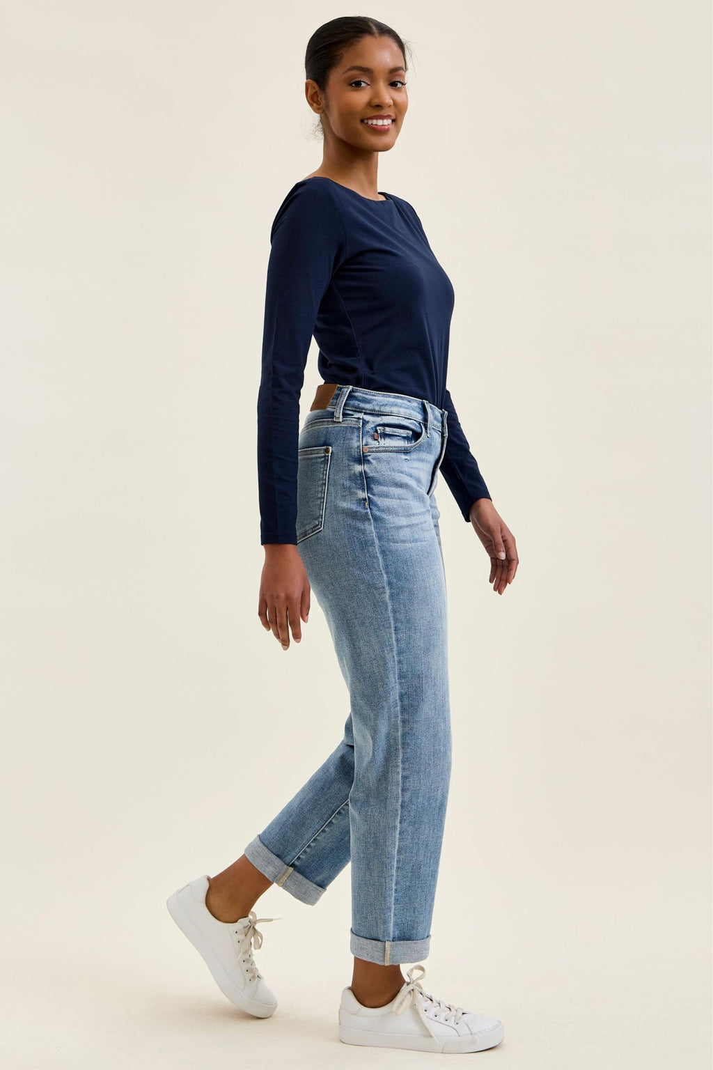 Woman wearing a navy long-sleeve top and light blue jeans on a beige background