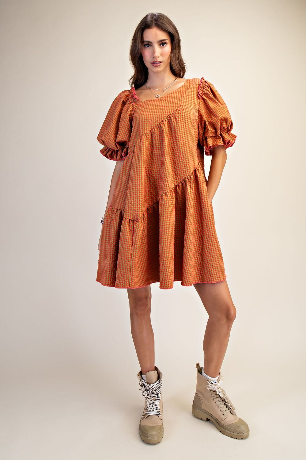 Woman wearing a rust-colored checkered dress with ruffled sleeves on a white background