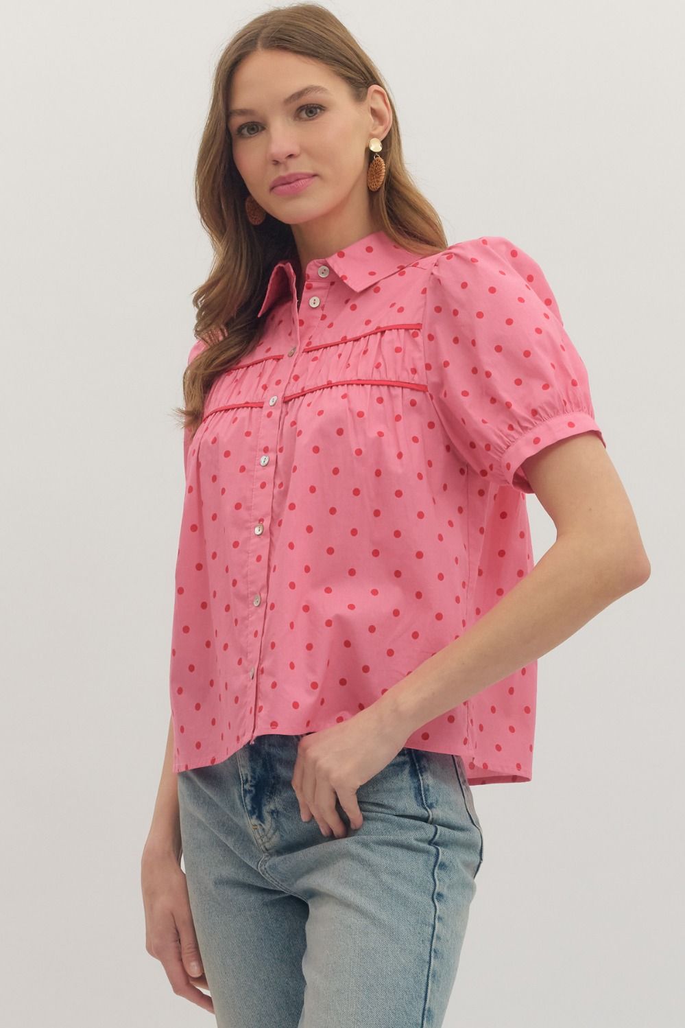Woman wearing a pink polka dot blouse with short sleeves on a plain background