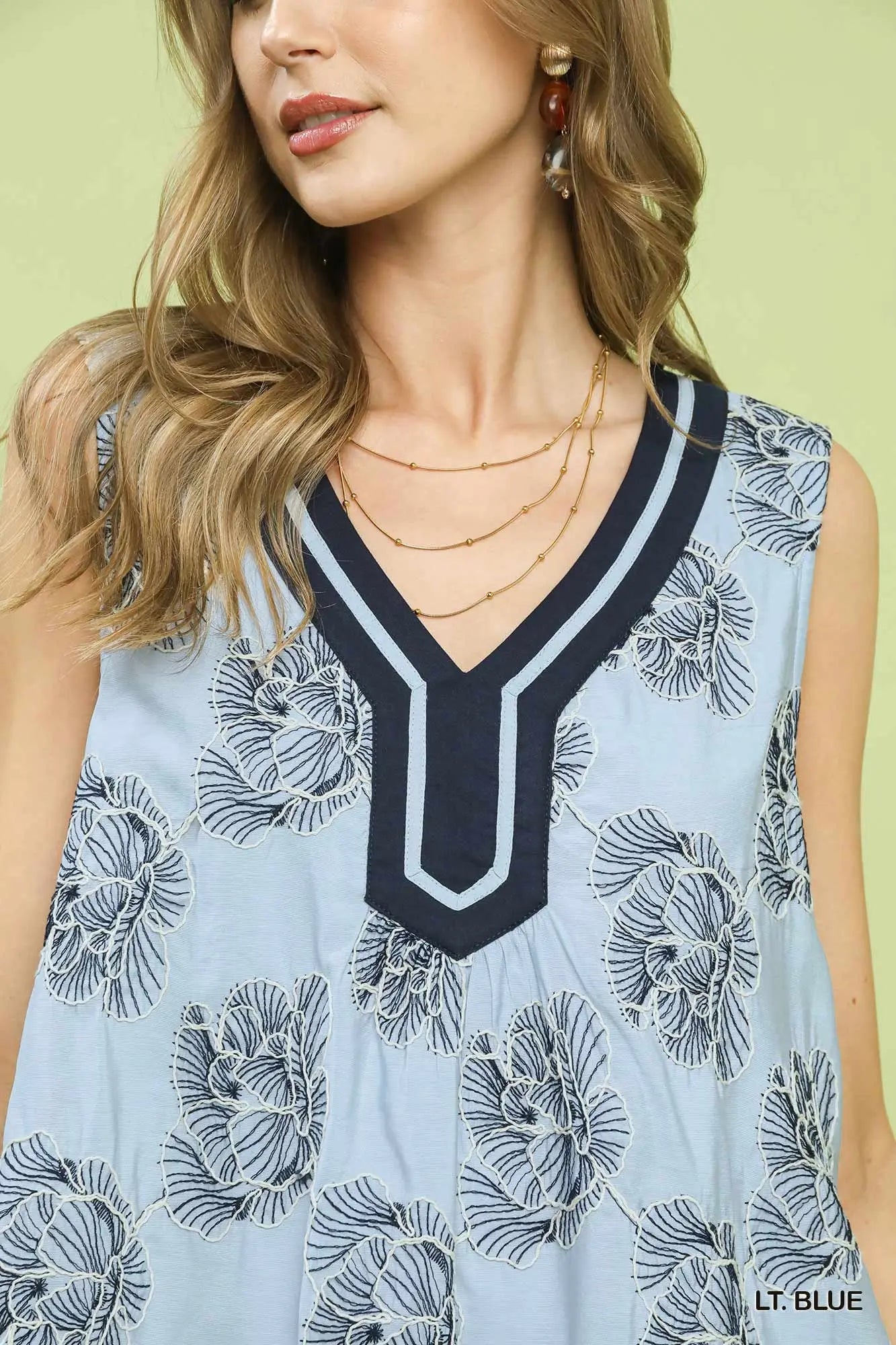 Light blue sleeveless top with black floral pattern and neckline detail on a model against a light green background.