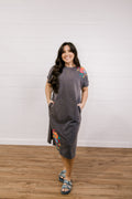 Woman wearing a gray dress with floral embroidery standing against a white wall.