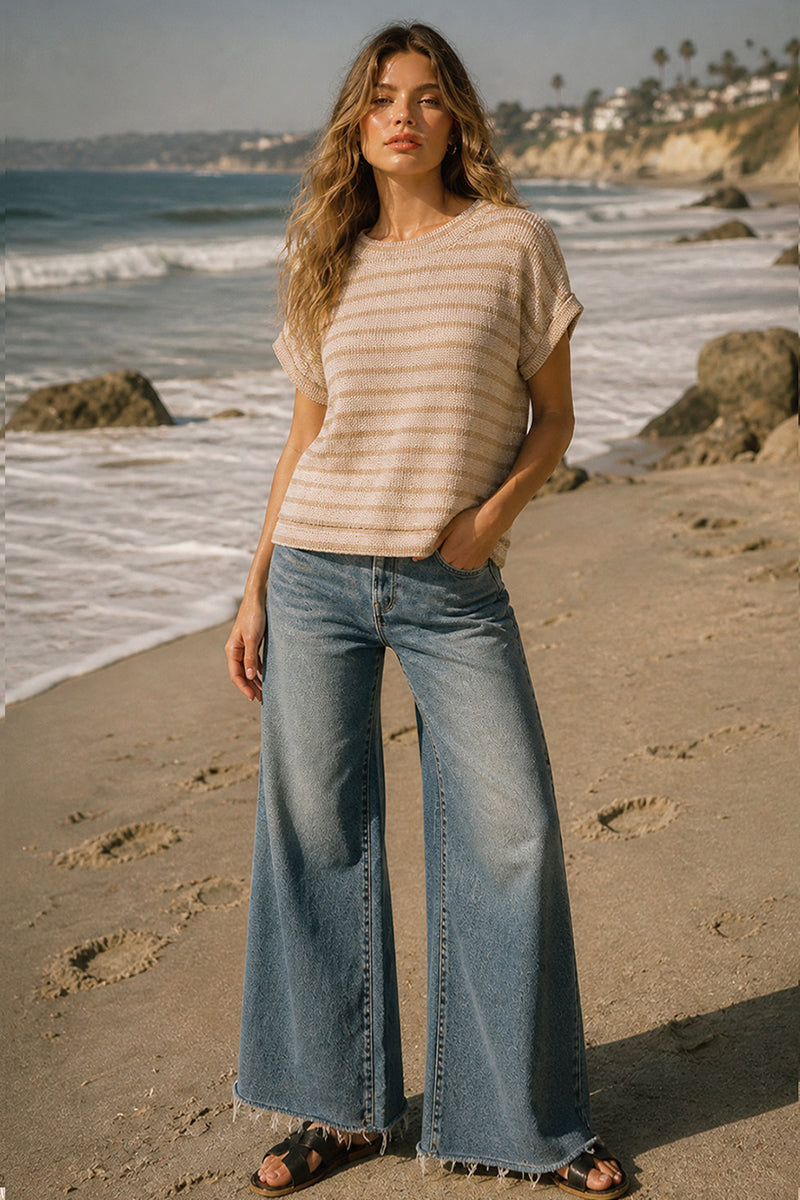 Woman standing on a beach wearing a striped shirt and wide-leg jeans.