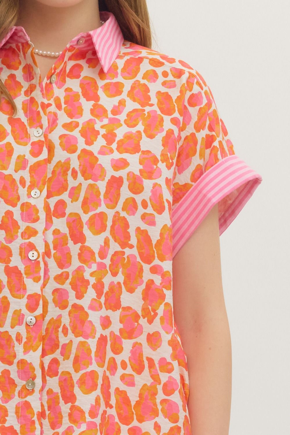 Person wearing a colorful patterned shirt with pink accents on a plain background