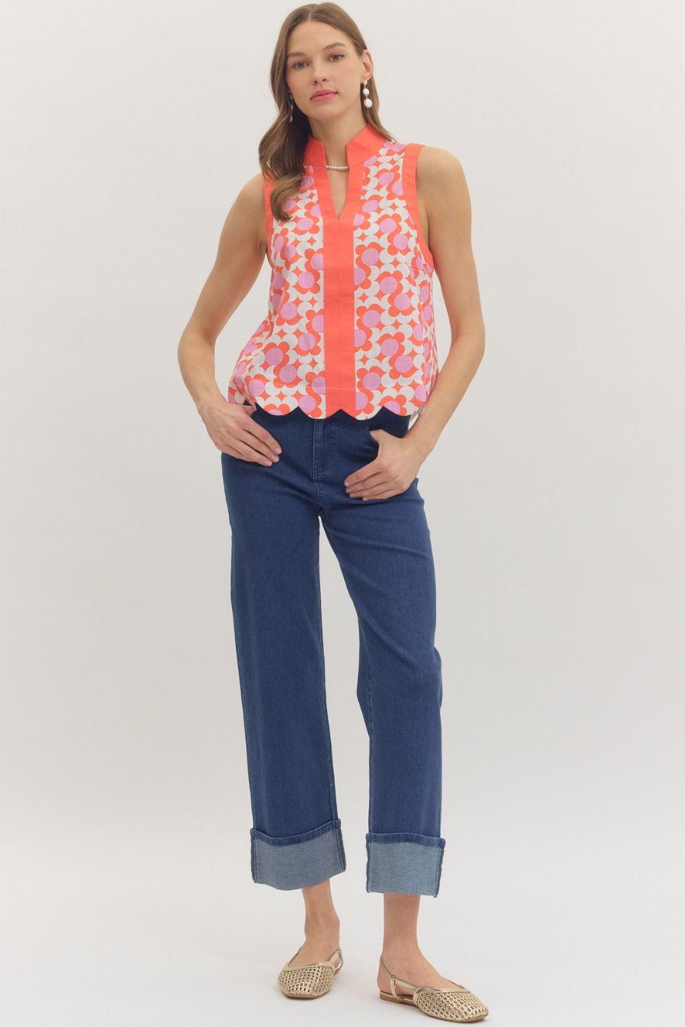 Woman wearing a sleeveless patterned top and blue jeans on a white background