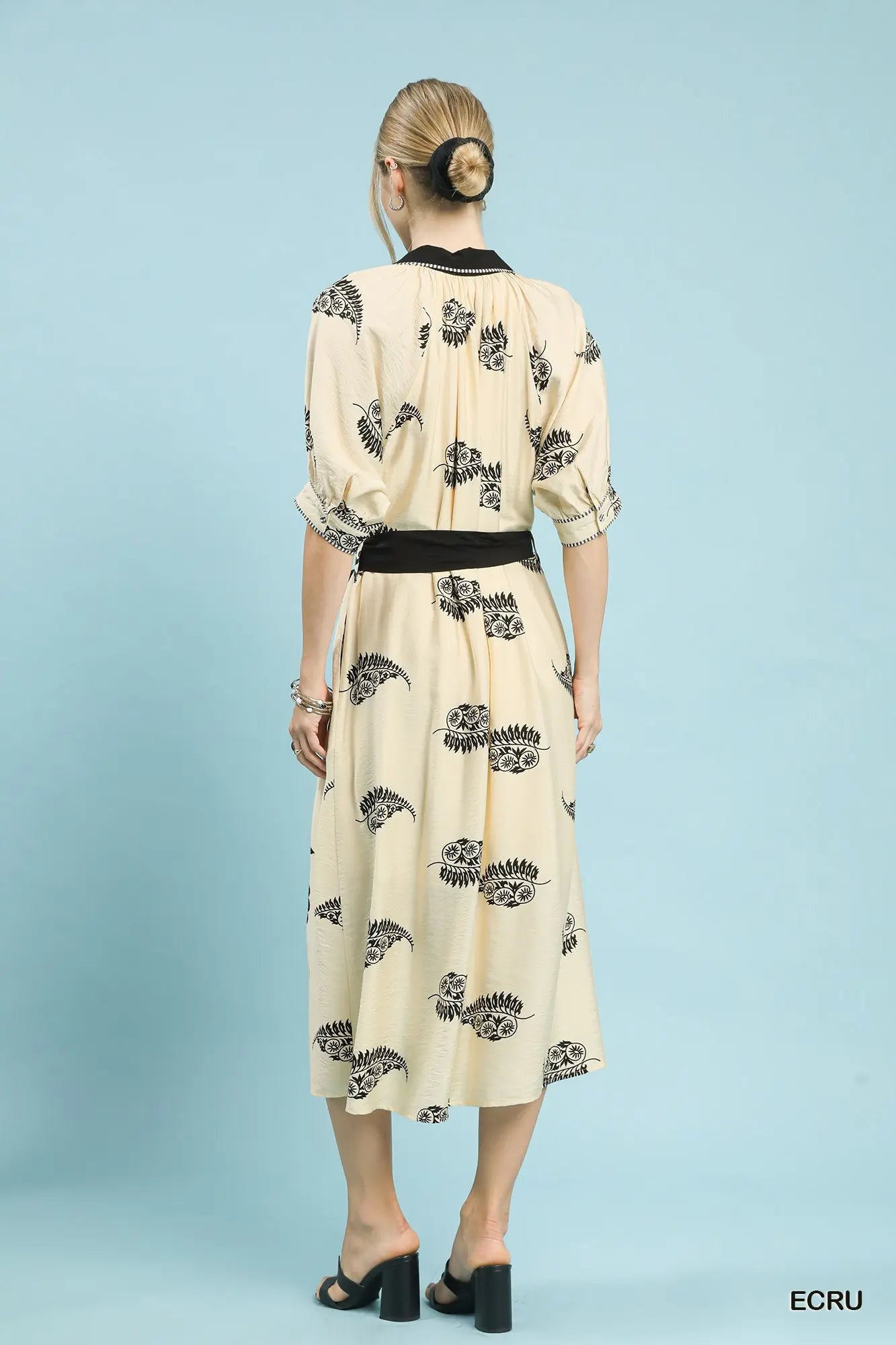 Woman wearing a cream dress with black floral pattern on a light blue background
