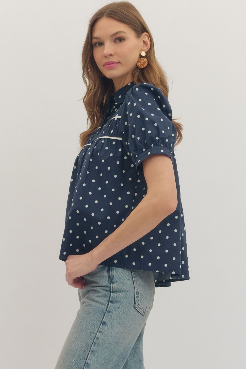 Woman wearing a navy blue shirt with white polka dots and light blue jeans on a plain background