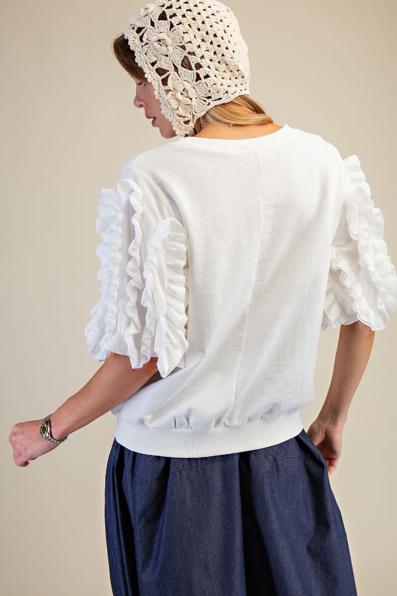 Person wearing a white blouse with ruffled sleeves and a matching white headscarf on a beige background