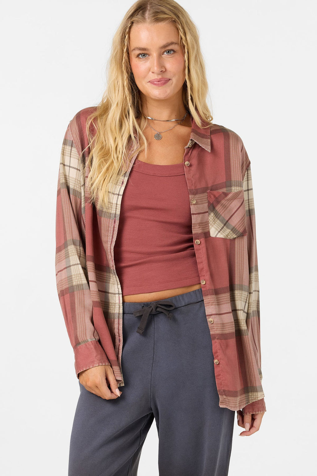 A woman modeling a rust-colored plaid button-up shirt over a matching ribbed tank top and dark gray drawstring sweatpants, photographed against a light gray studio background.