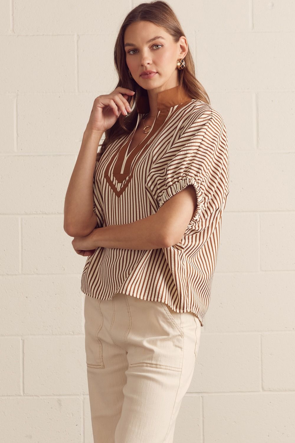 Woman wearing a striped blouse and beige pants against a light background