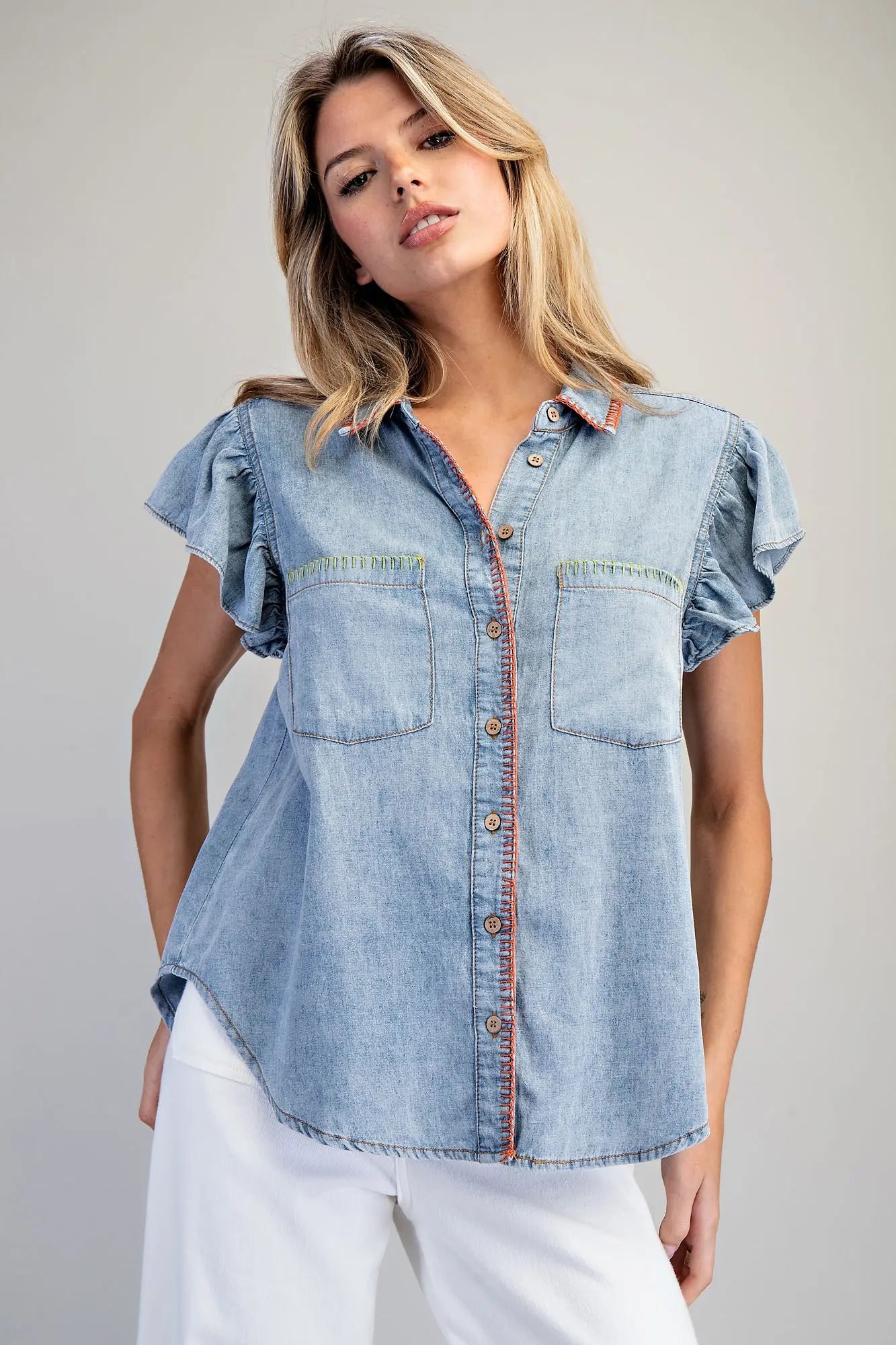 Woman wearing a light blue denim shirt with ruffled sleeves on a plain background