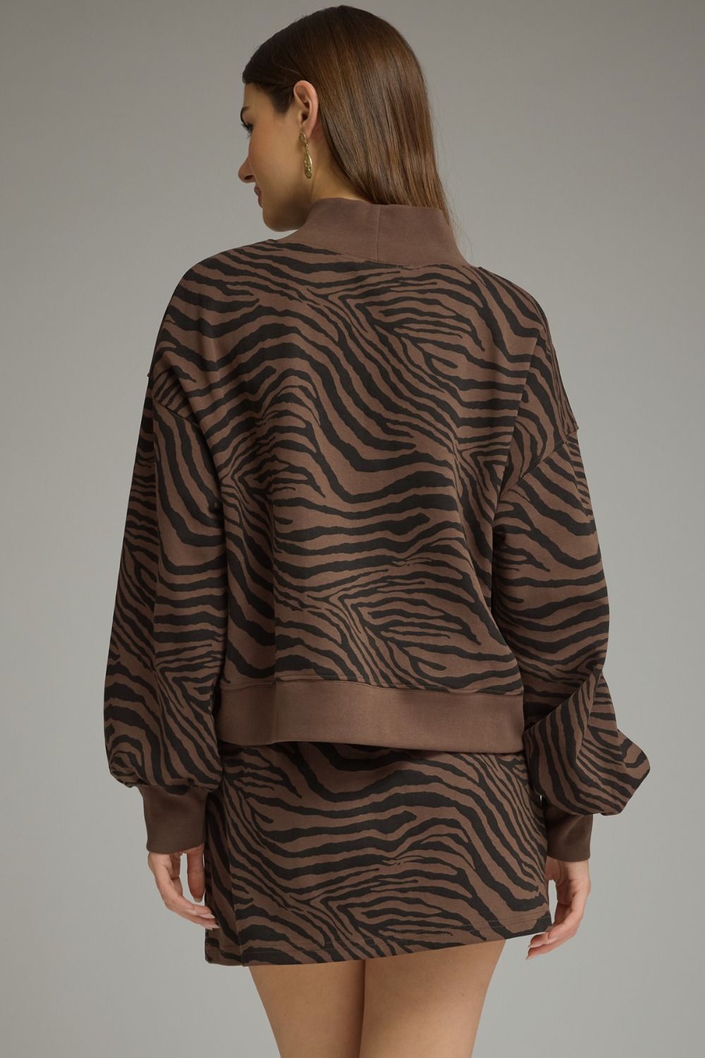 A woman shown from the back wearing a brown and black zebra-print long-sleeve top and matching mini skirt against a solid gray studio background.
