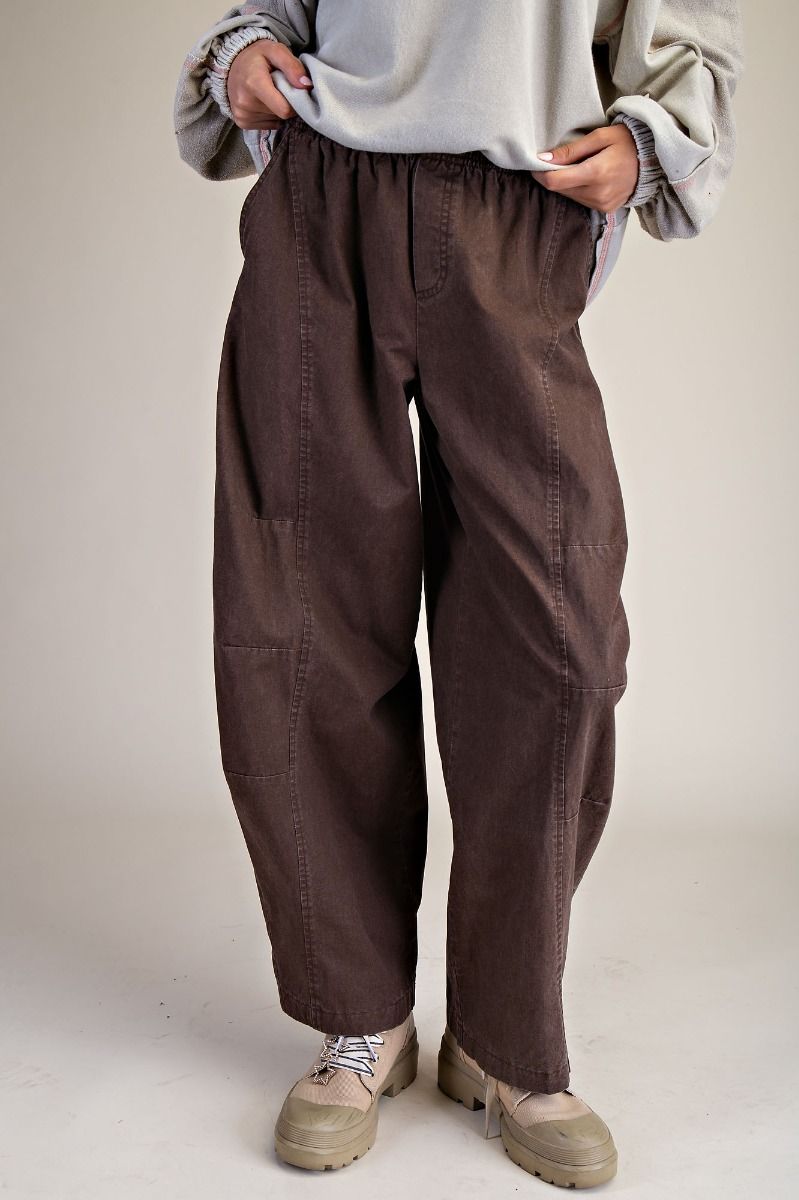 Person wearing brown baggy pants and beige shoes on a plain background
