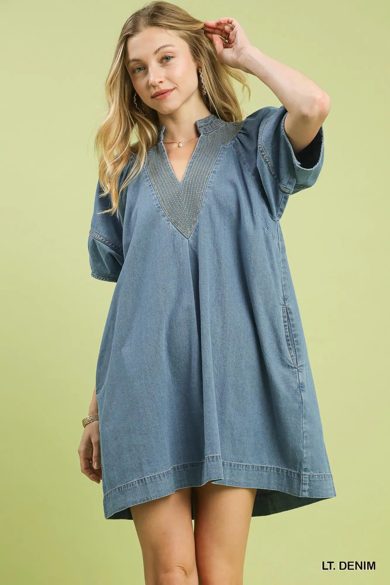 Woman wearing a light denim dress against a light green background