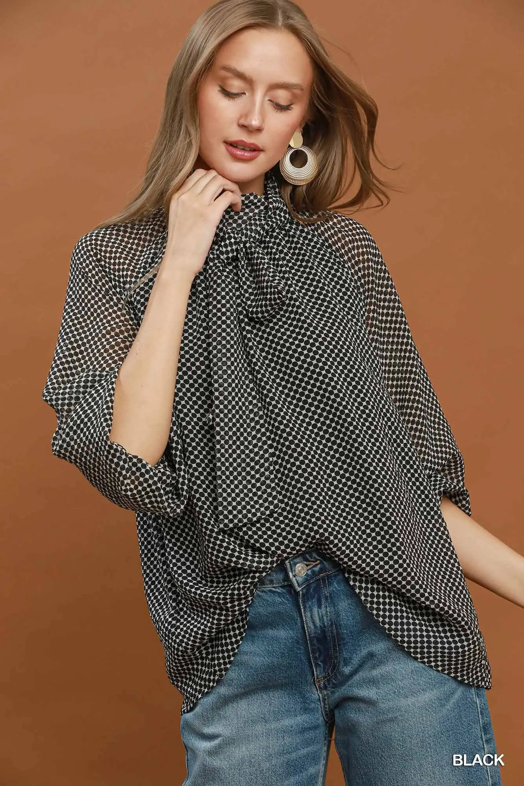 Woman wearing a black and white checkered poncho over a black top with blue jeans on a brown background
