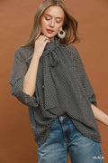 Woman wearing a black and white checkered poncho over a black top with blue jeans on a brown background