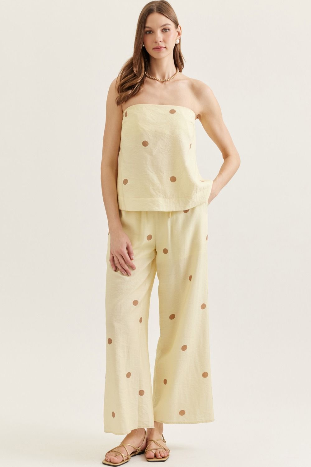 Woman wearing a yellow polka dot top and pants on a white background