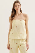 Woman wearing a light yellow strapless top and pants with button details on a plain background
