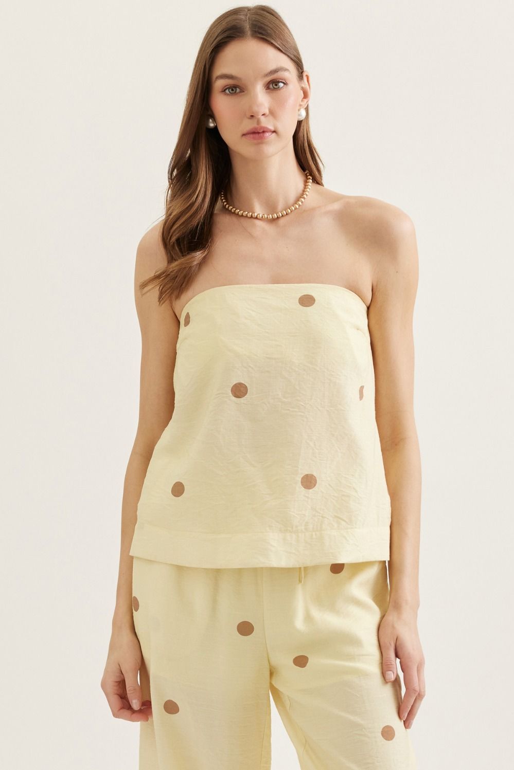 Woman wearing a light yellow strapless top and pants with button details on a plain background