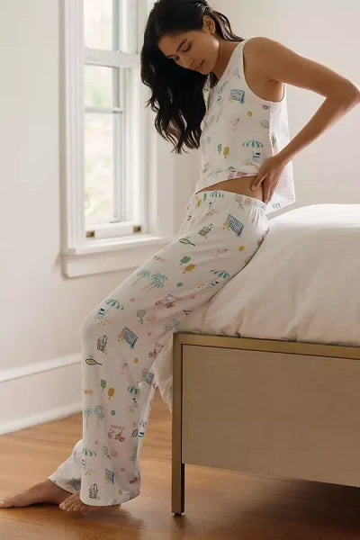 Woman wearing a white tank top and pajama set with cartoon designs, sitting on a bed.