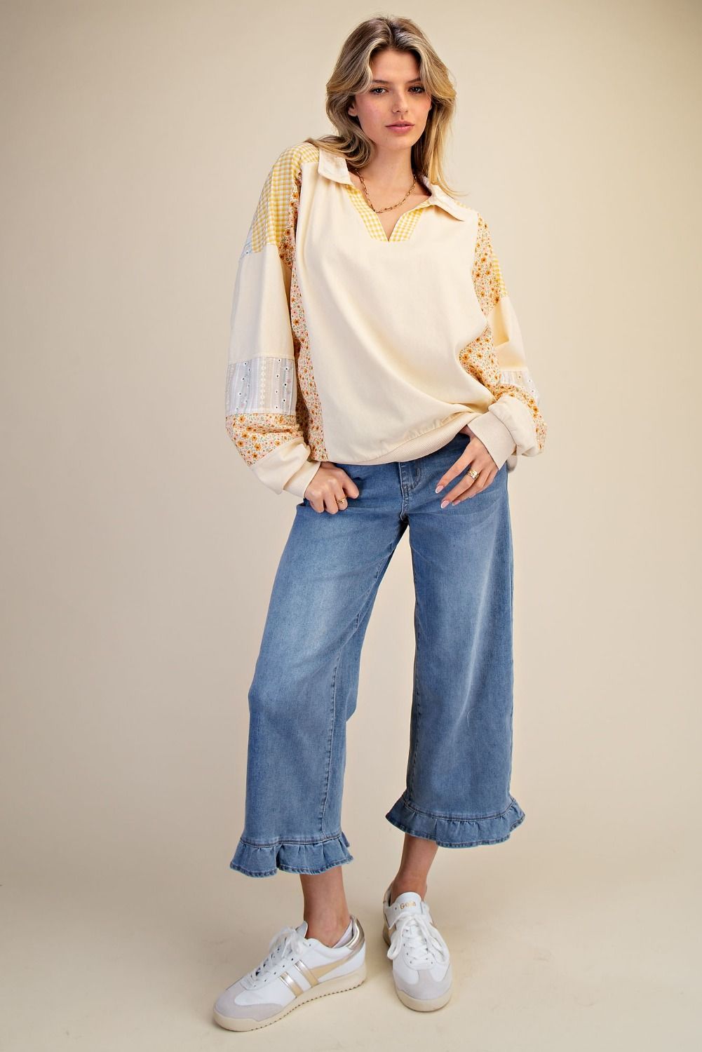 Woman wearing a cream jacket, white shirt, blue jeans, and white sneakers on a beige background