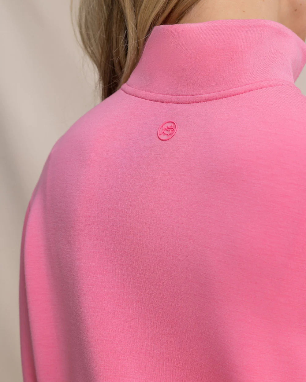 Close-up of a pink garment with a brand logo on a neutral background