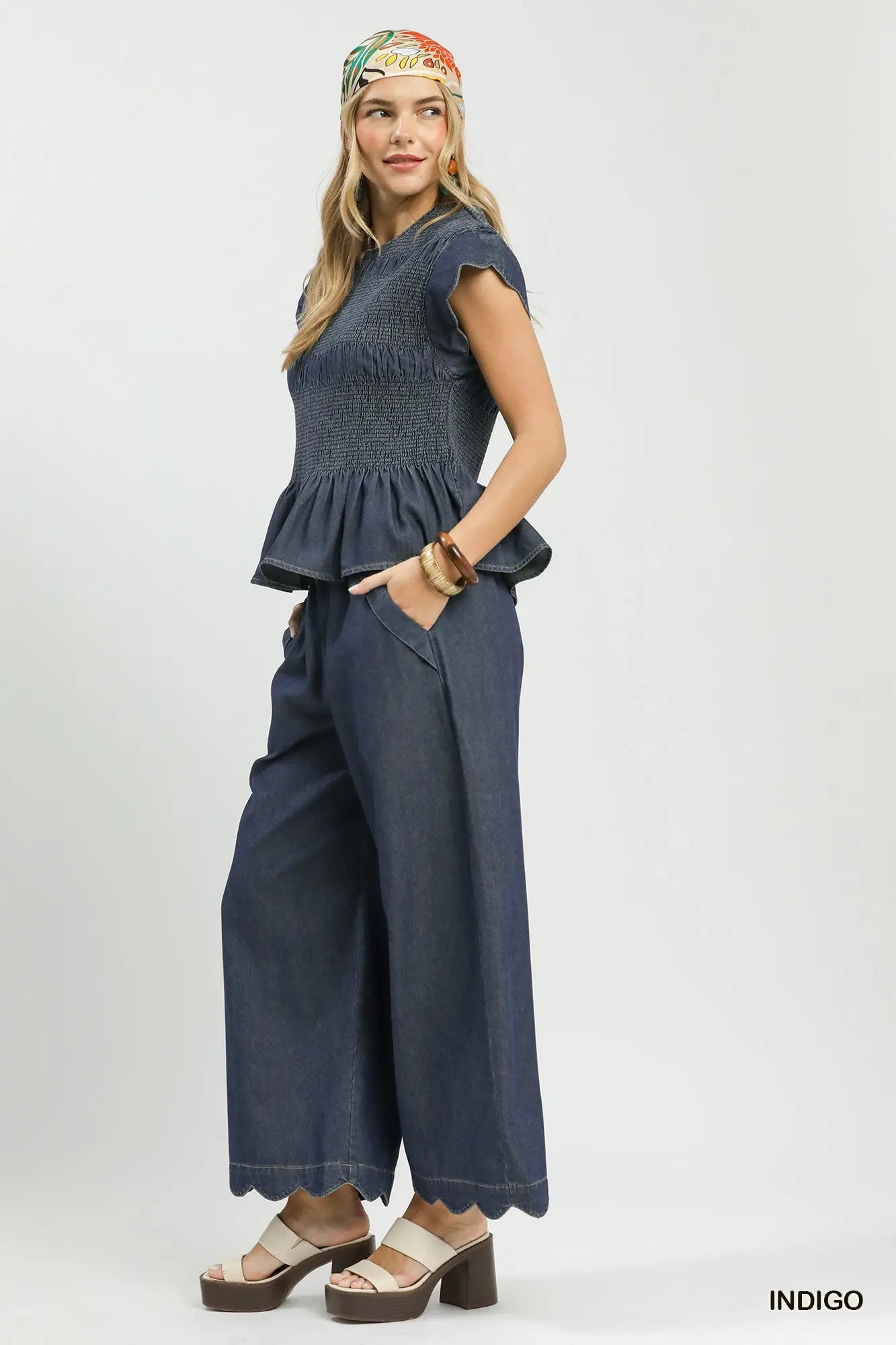 Woman wearing a blue peplum top and wide-leg pants with a colorful headband on a white background.