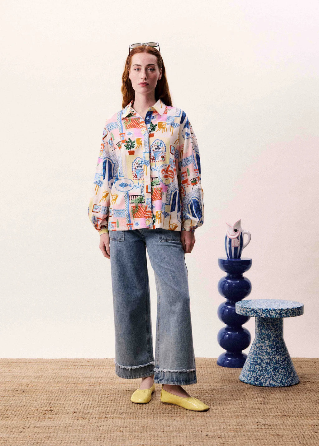 Person wearing a colorful patterned shirt and jeans standing in a room with decorative elements.