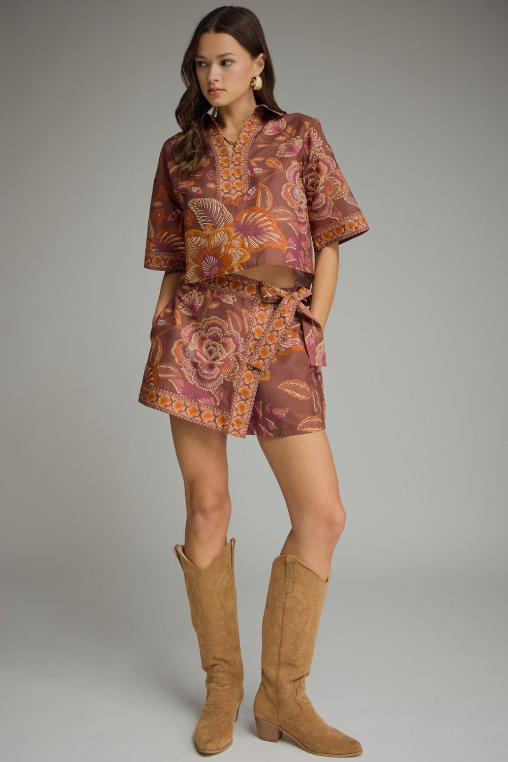 Woman wearing a patterned outfit with high boots on a plain background