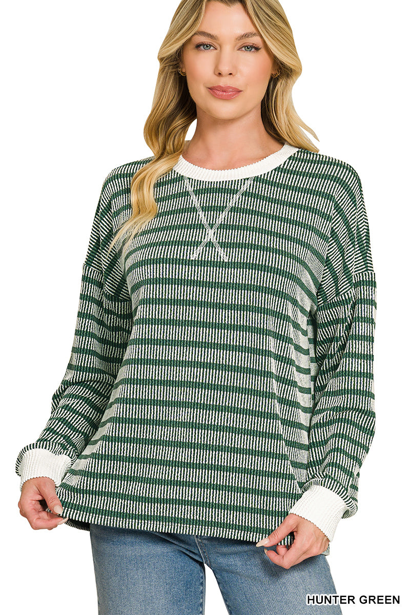 A woman modeling a long-sleeve knit top with horizontal green and white stripes, featuring a white crew neck and white ribbed cuffs, paired with blue jeans against a plain white background.