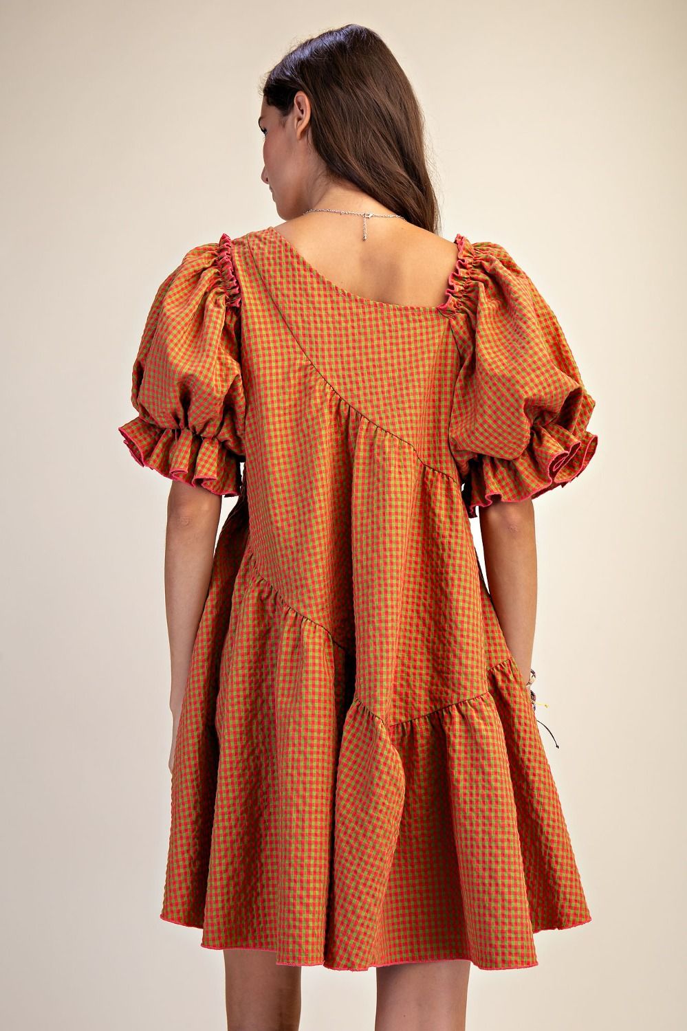 Woman wearing an orange checkered dress with ruffled sleeves on a beige background
