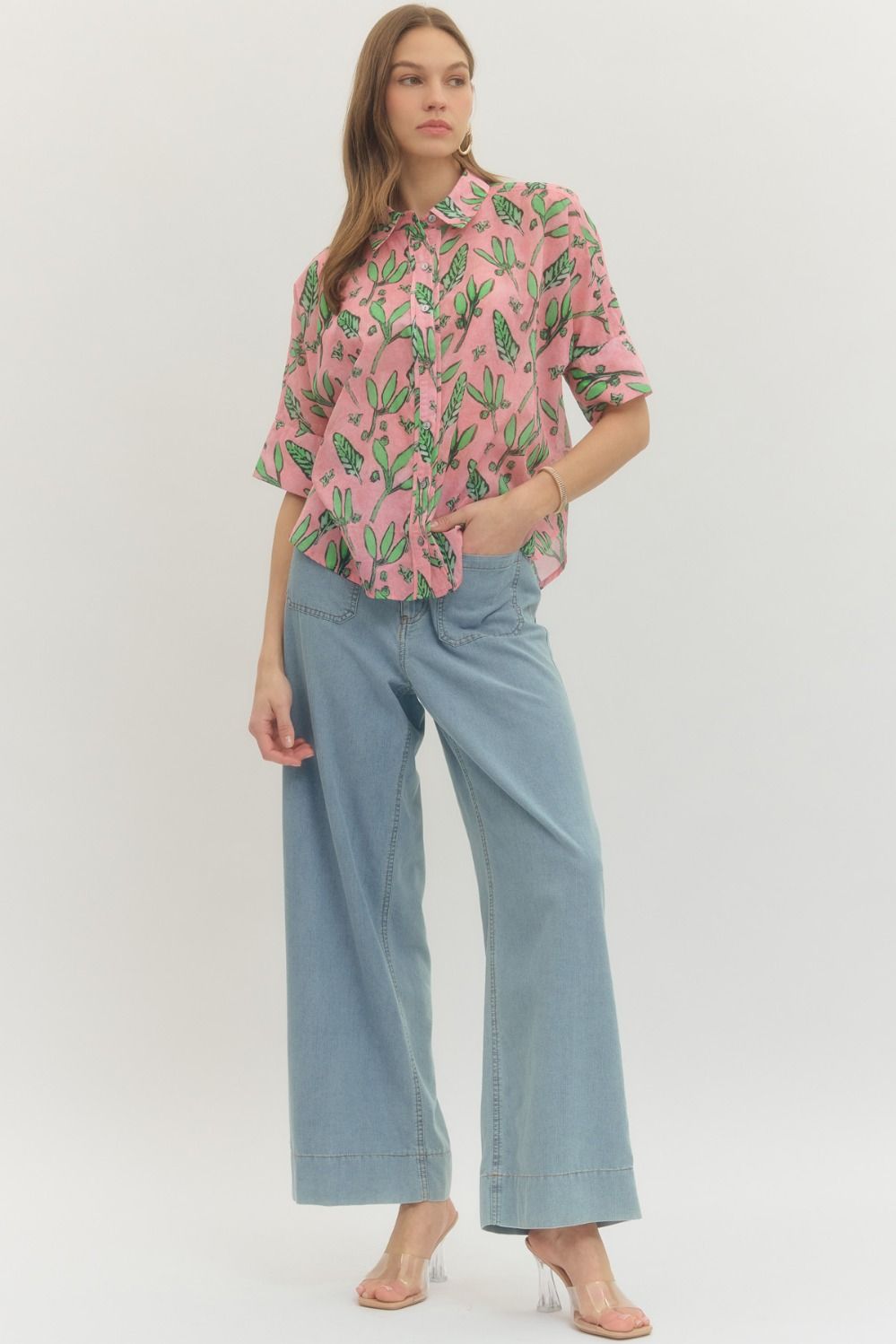 Woman wearing a pink cactus-patterned shirt and light blue jeans on a white background