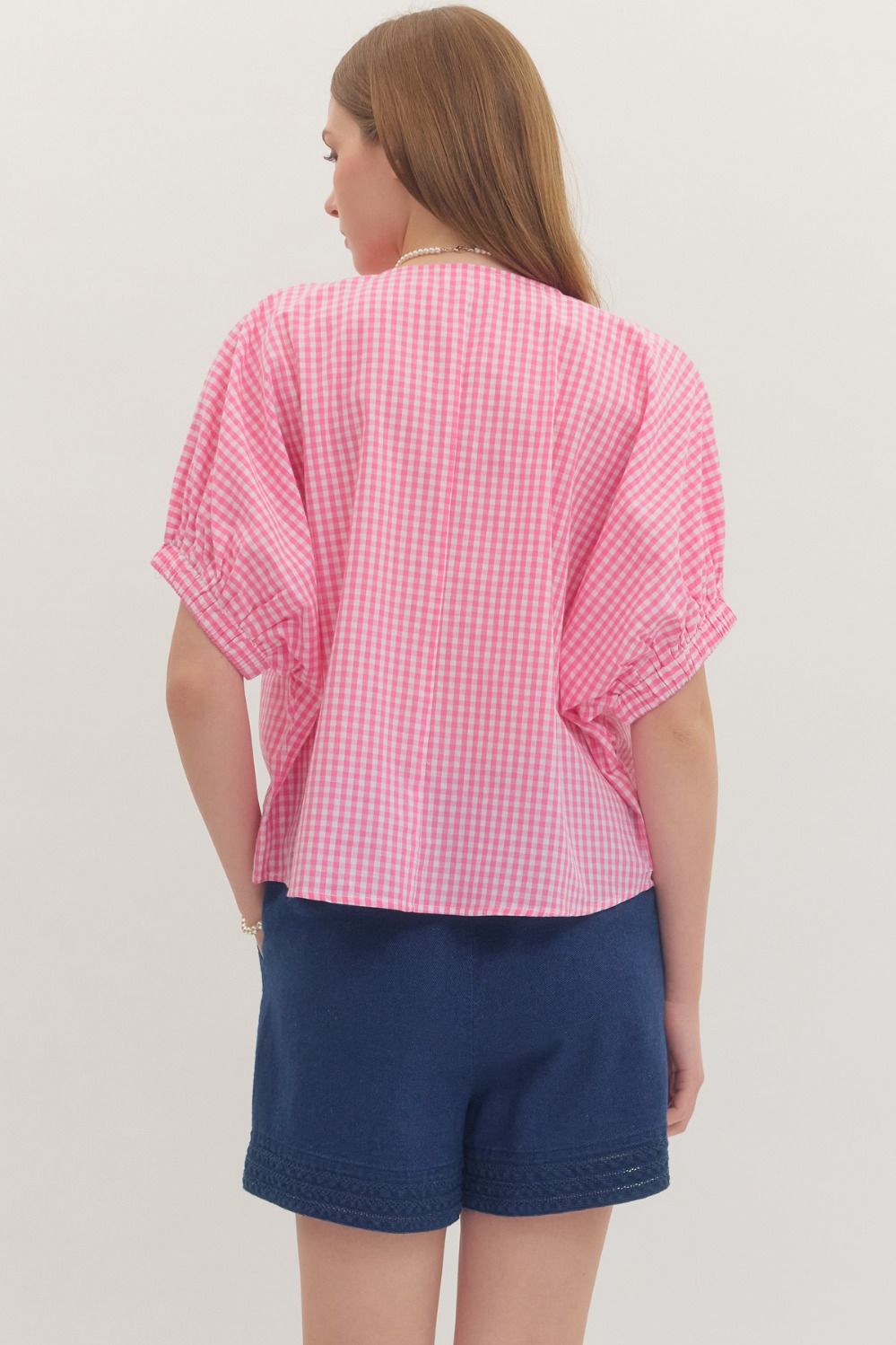Person wearing a pink checkered shirt and blue shorts on a plain background