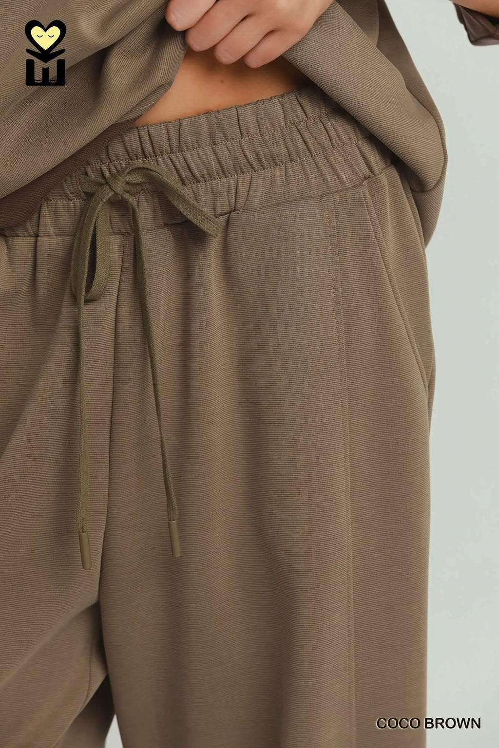 Close-up of brown pants with a tie waist on a light gray background
