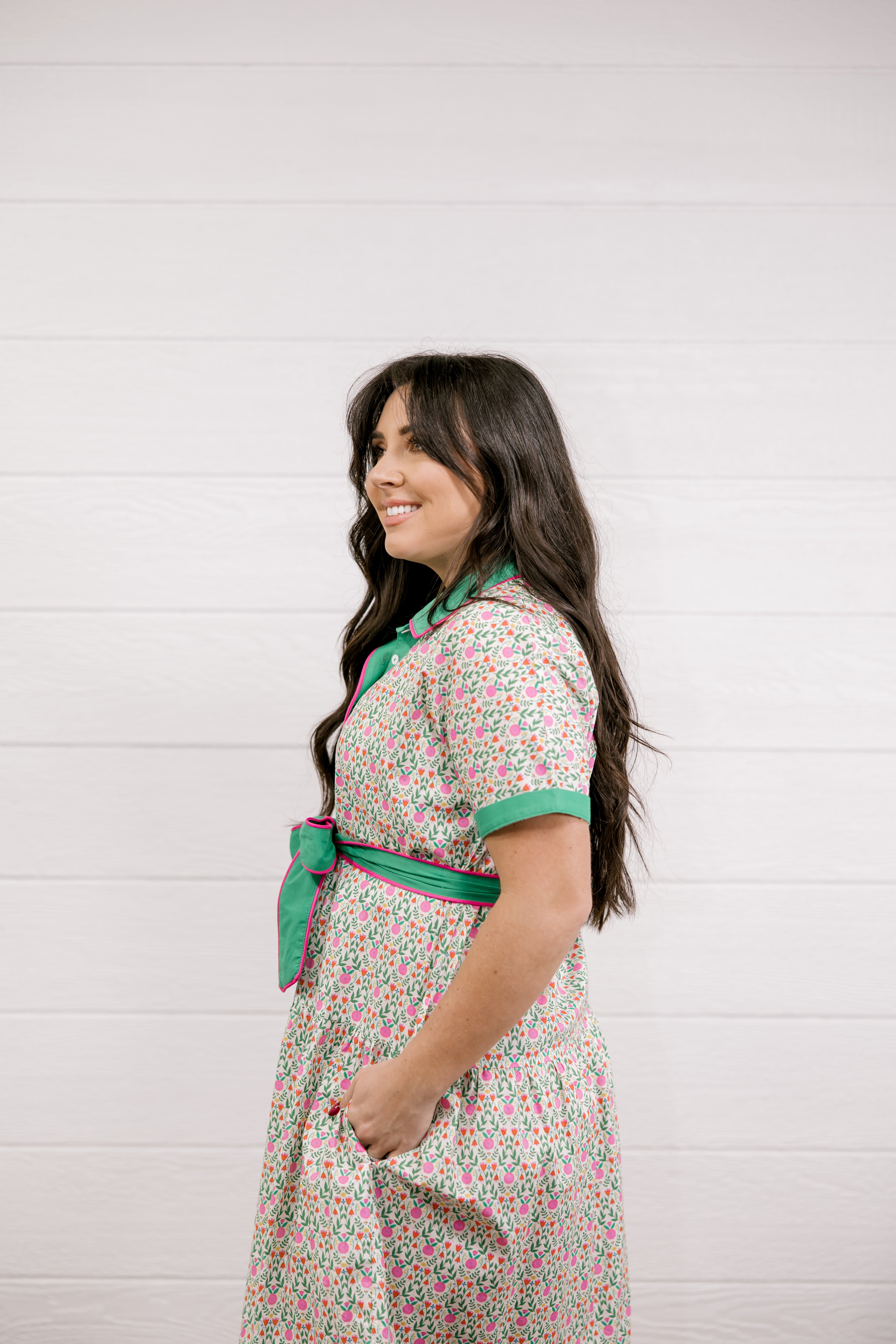 Woman wearing a floral dress with a green belt against a white background
