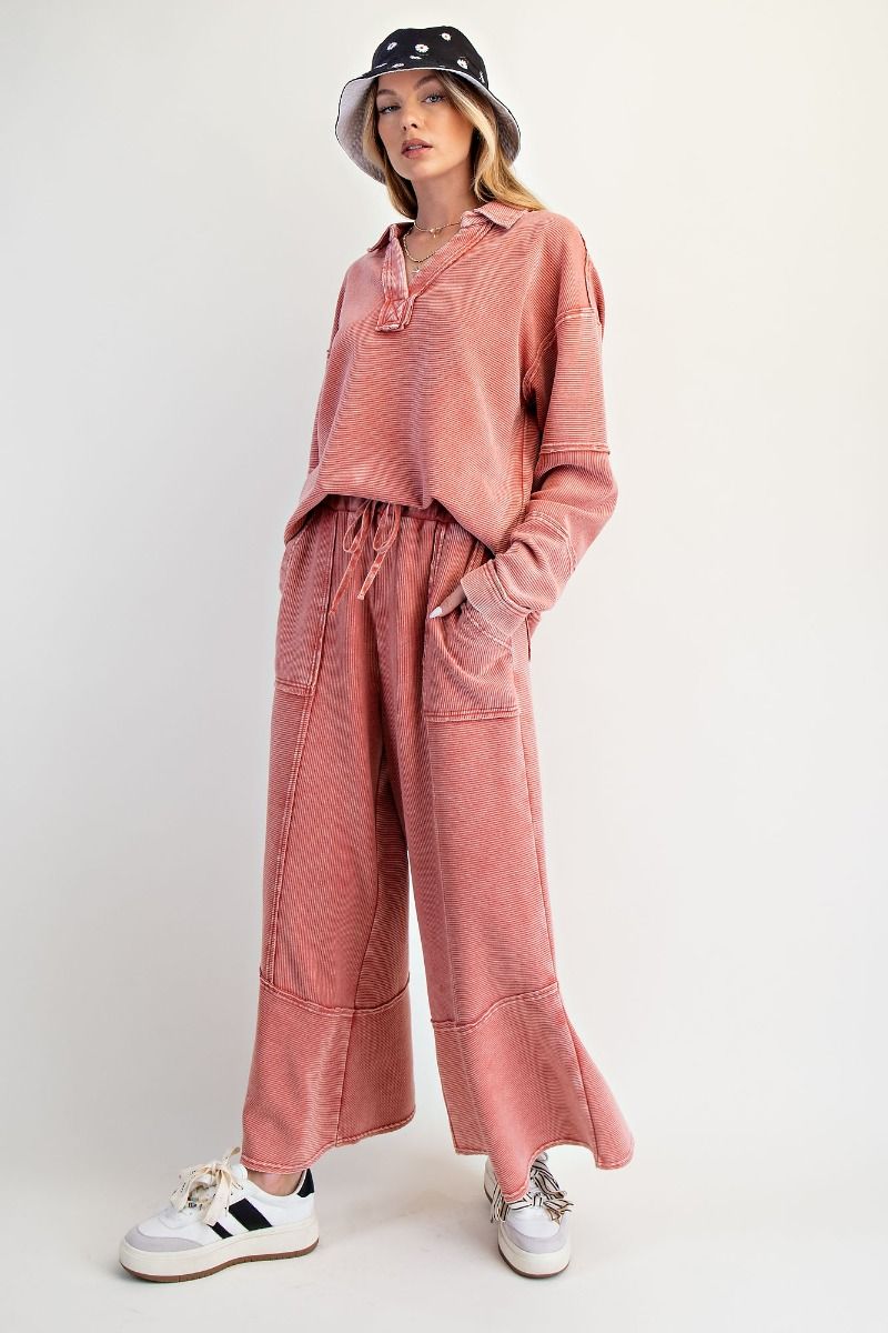 Person wearing a pink outfit with wide-leg pants and a matching top, standing against a white background.