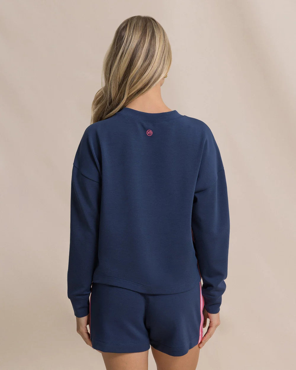 Person wearing a navy blue sweatshirt and shorts set on a beige background