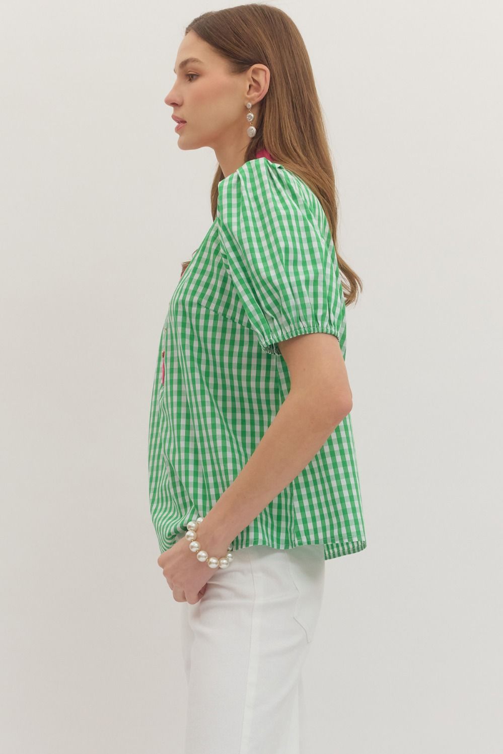 Woman wearing a green checkered shirt and white pants on a plain background