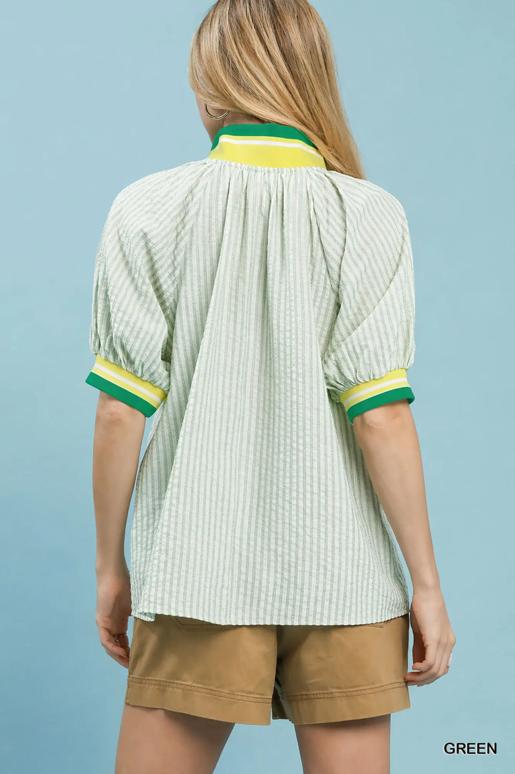Woman wearing a light green blouse with yellow and green trim on a blue background