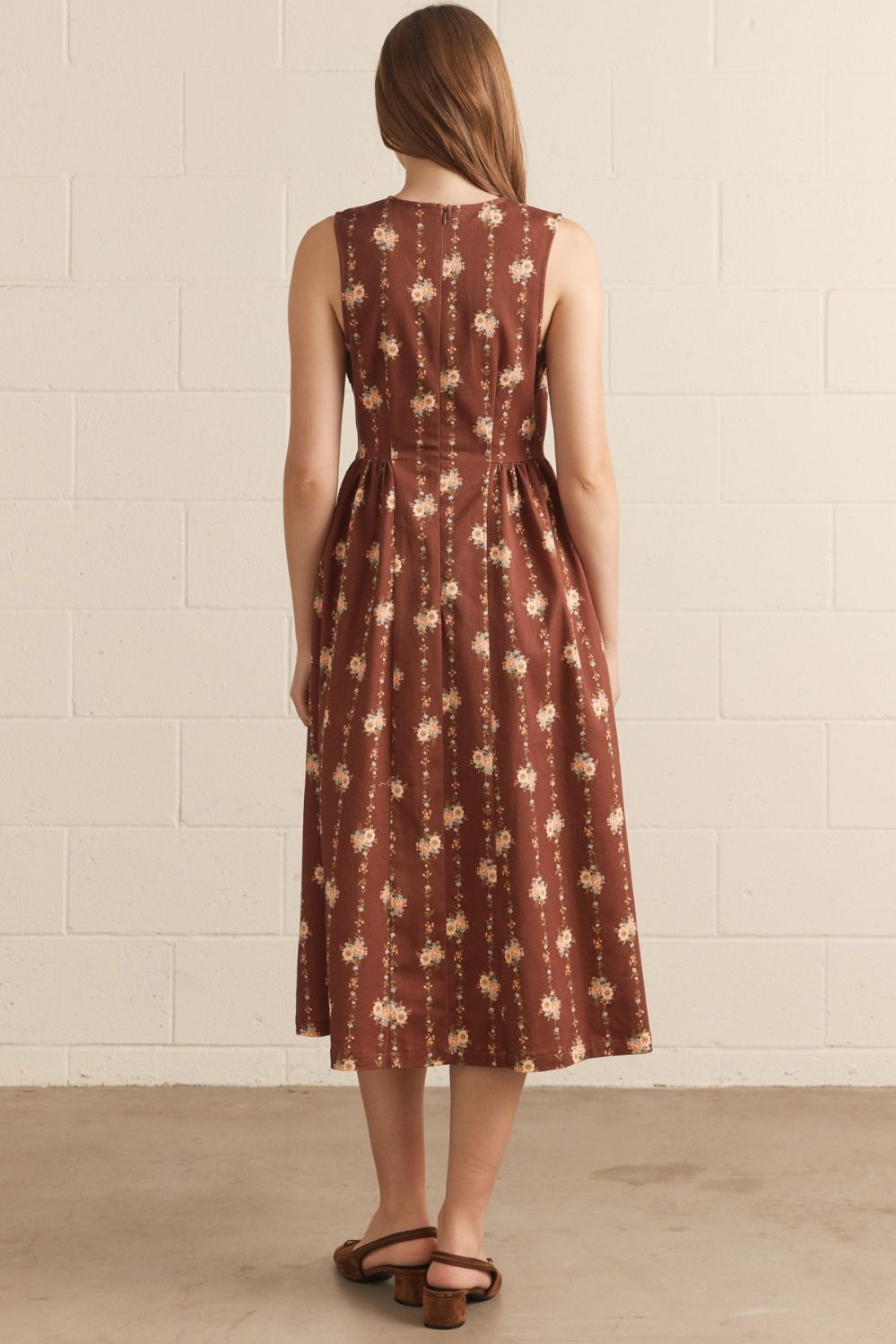 Woman wearing a brown floral dress against a white tiled wall.